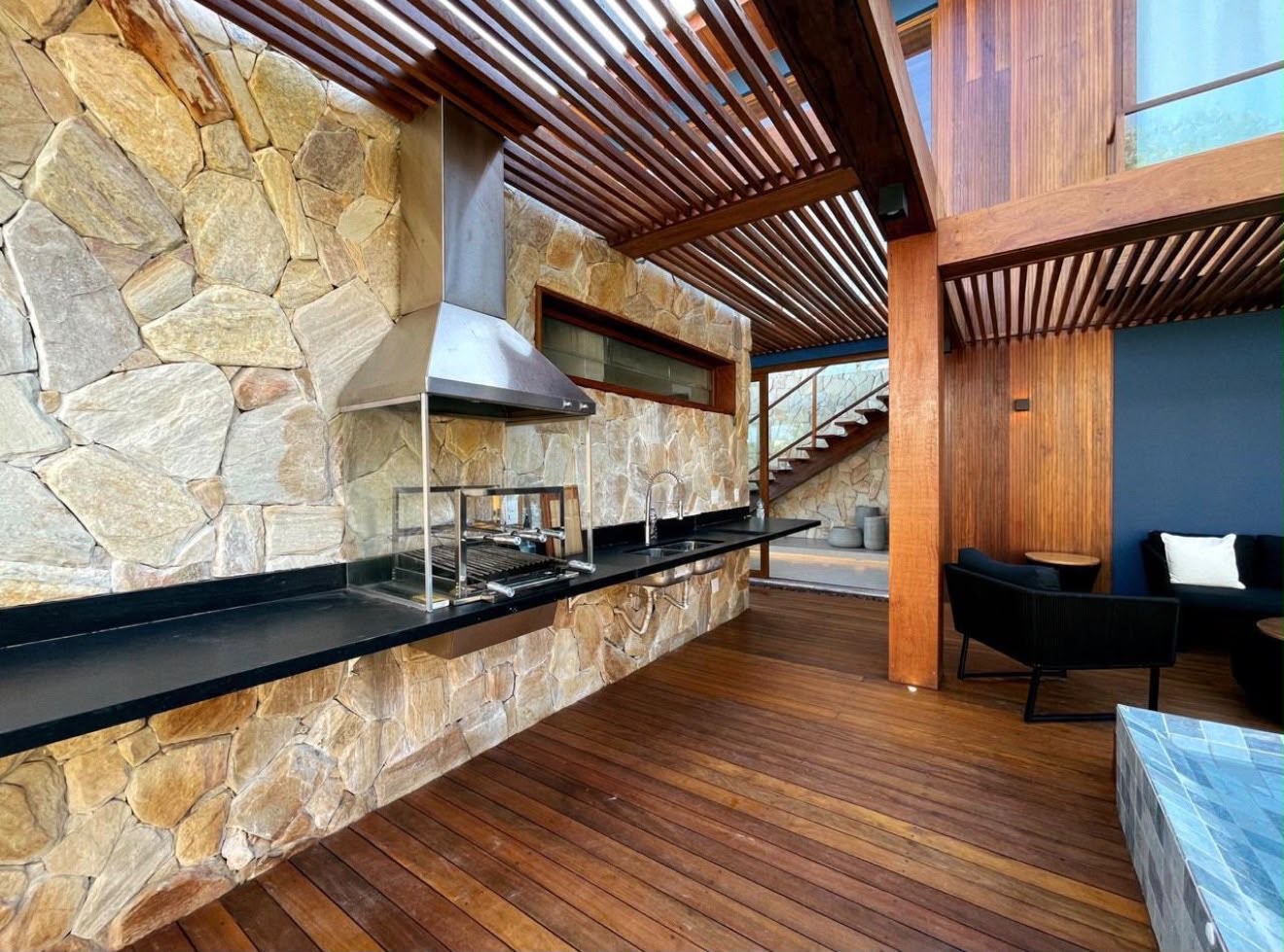 Espaço gourmet com churrasqueira, parede de pedra e pergolado de madeira
